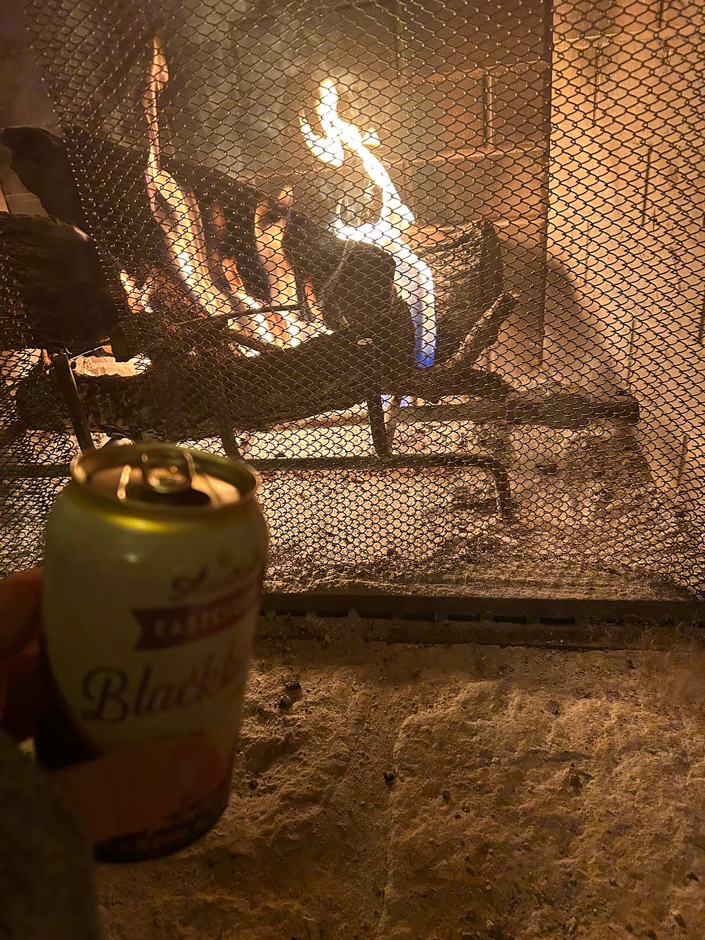 A can of Blackberry Cider front left, lit fireplace in the background.