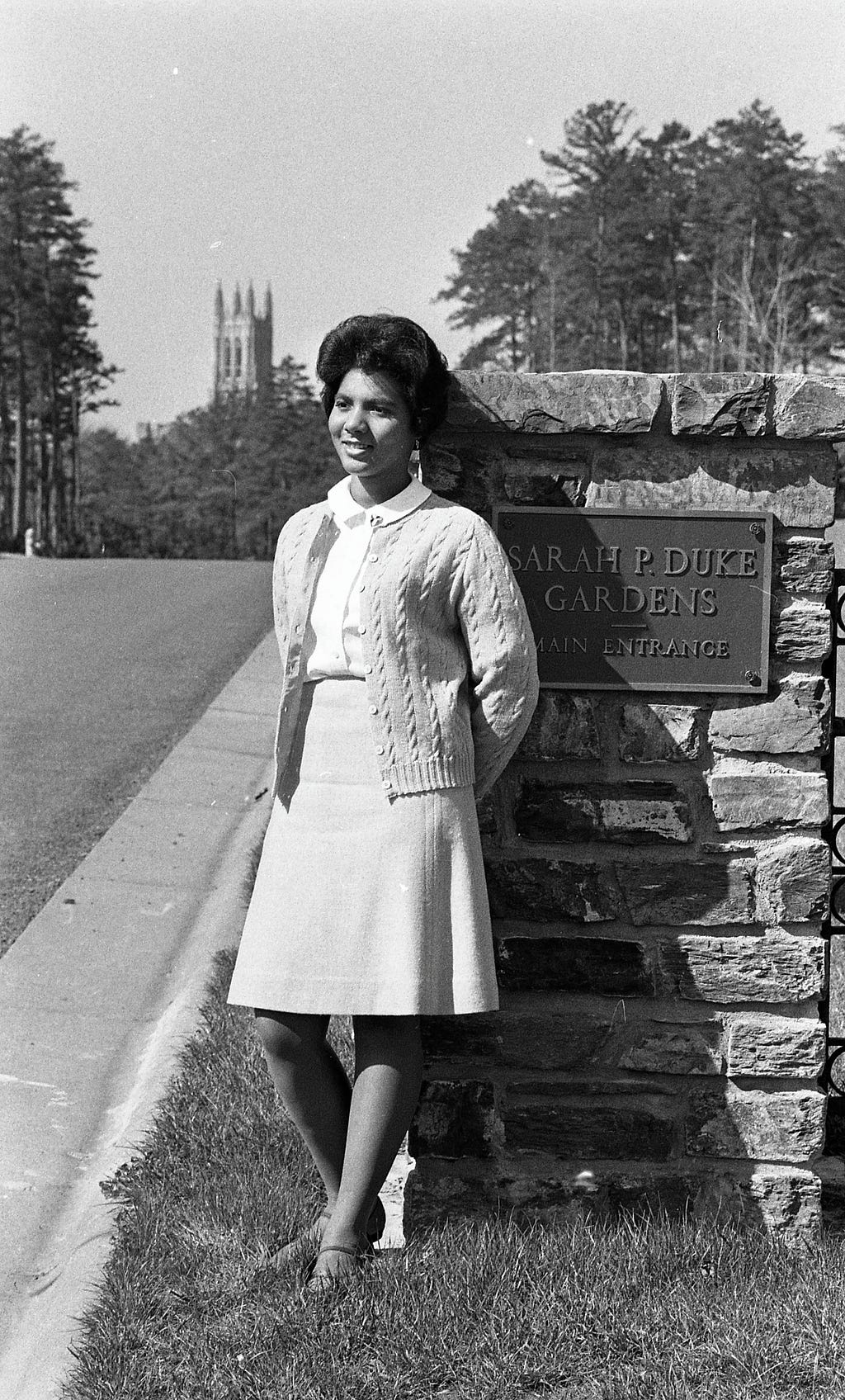 Wilhelmina Reuben, May Queen 1967, leans on a stone column with a plaque that says, “Sarah P. Duke Gardens, Main Entrance.”