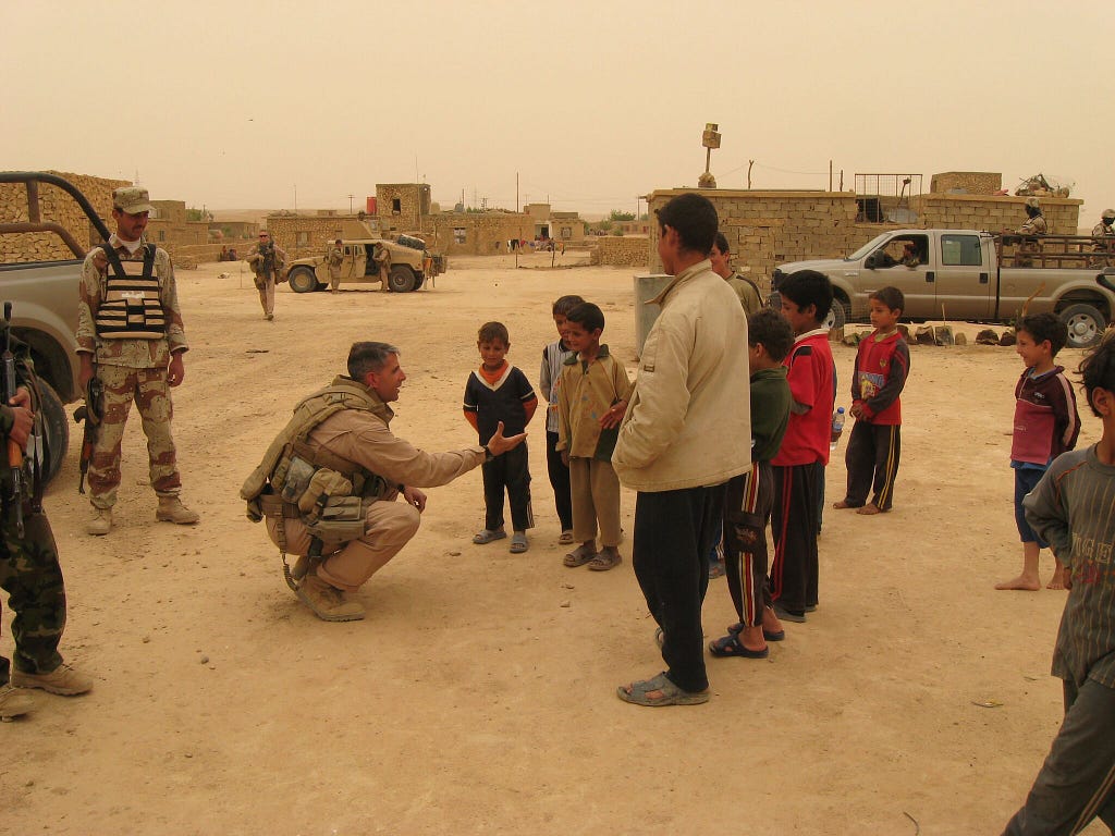 Man in military uniform shakes hands with Iraq children