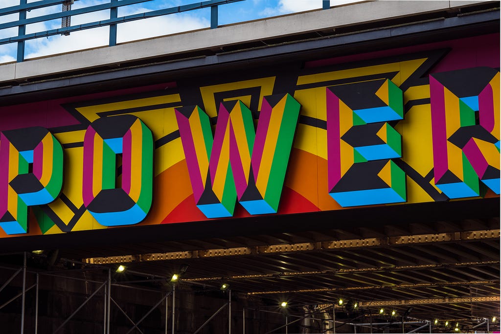 Colorful sign in bright yellow, green, blue, purple, red, orange, and gray outlines reads “POWER” in all capital letters.