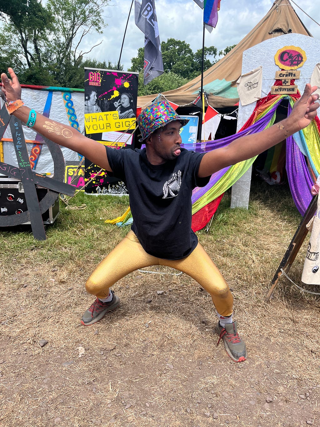 Man in gold tights holding a disco pose outside a colourful tent