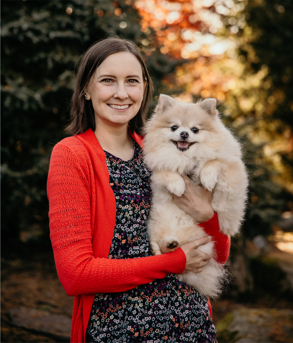 A smiling Kelly in a bright red sweater holds her grinning dog. Both stare into the camera, posing for the picture.