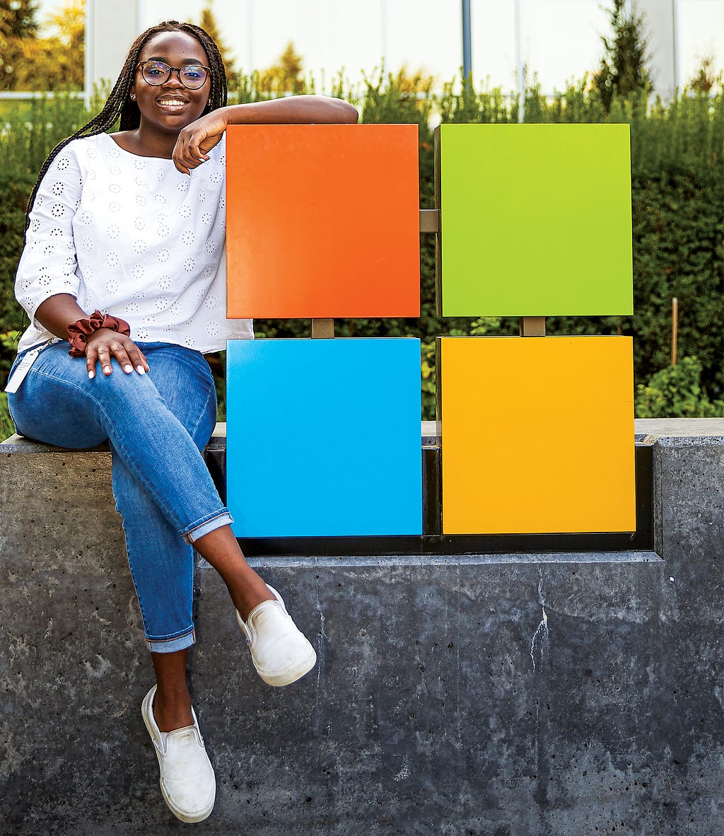 A young woman sits next to the iconic Microsoft logo and symbol.