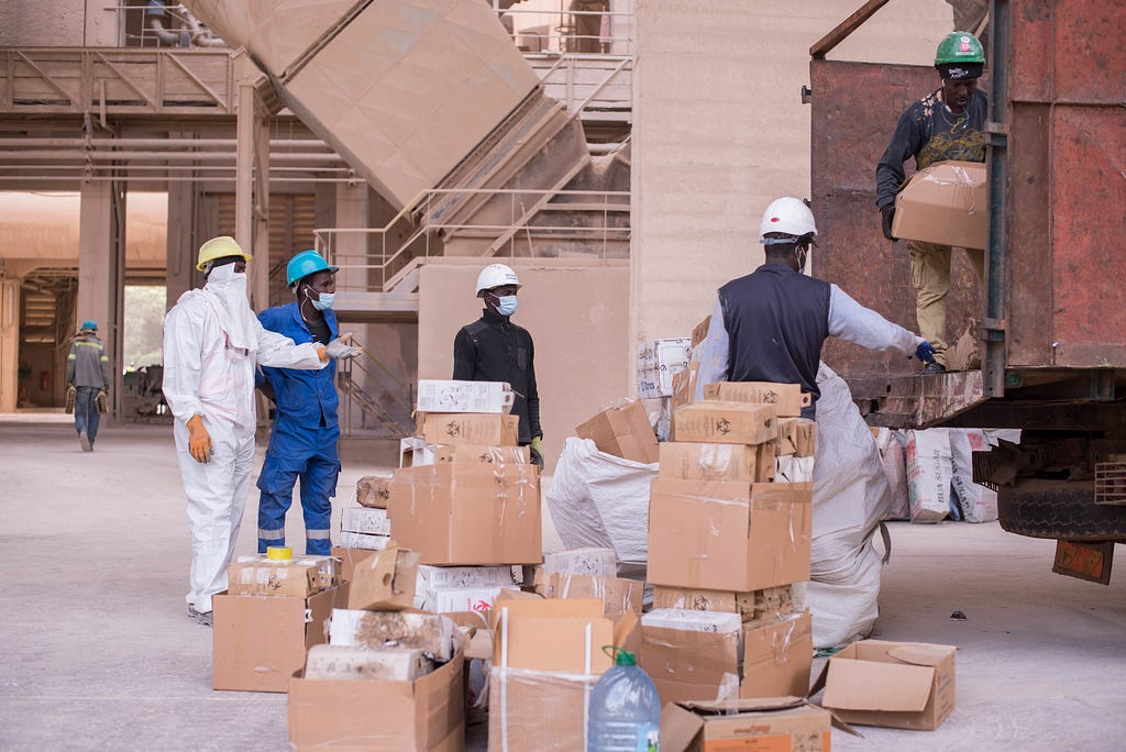 Men wearing masks and hardhats unload boxes from the back of a large truck.