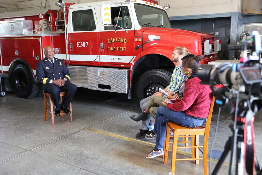 Three young adults sit down with Oakland Fire Chief Reginald Freeman at a local fire station.