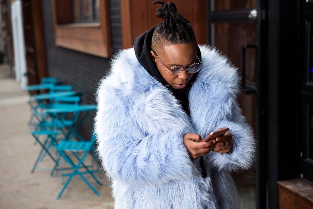 A person with a faux fur coat on looking down at their phone