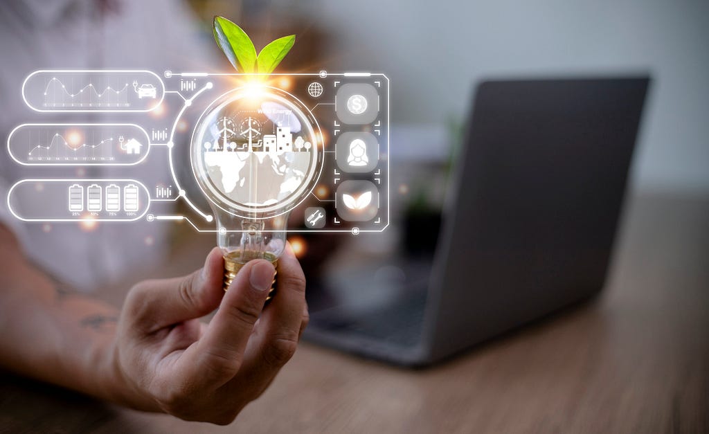 Business person’s hand holding a light bulb with a plant growing out of it, and an open laptop is in front of them. Graphics depicting a globe with windmills and carbon emission graphs are on the virtual screen.