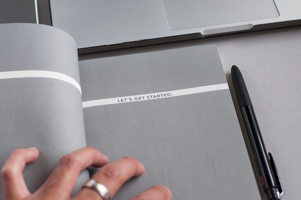 A notebook that says ‘let’s get started’ with a person’s hand on it