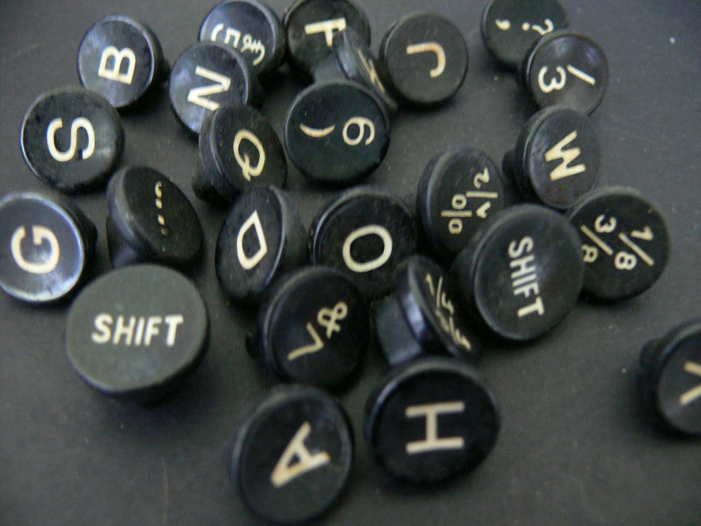 about 25 round keys from a typewriter (with letters, numbers, and punctuation on them) that have been removed from the typewriter and are lying randomly on a black surface