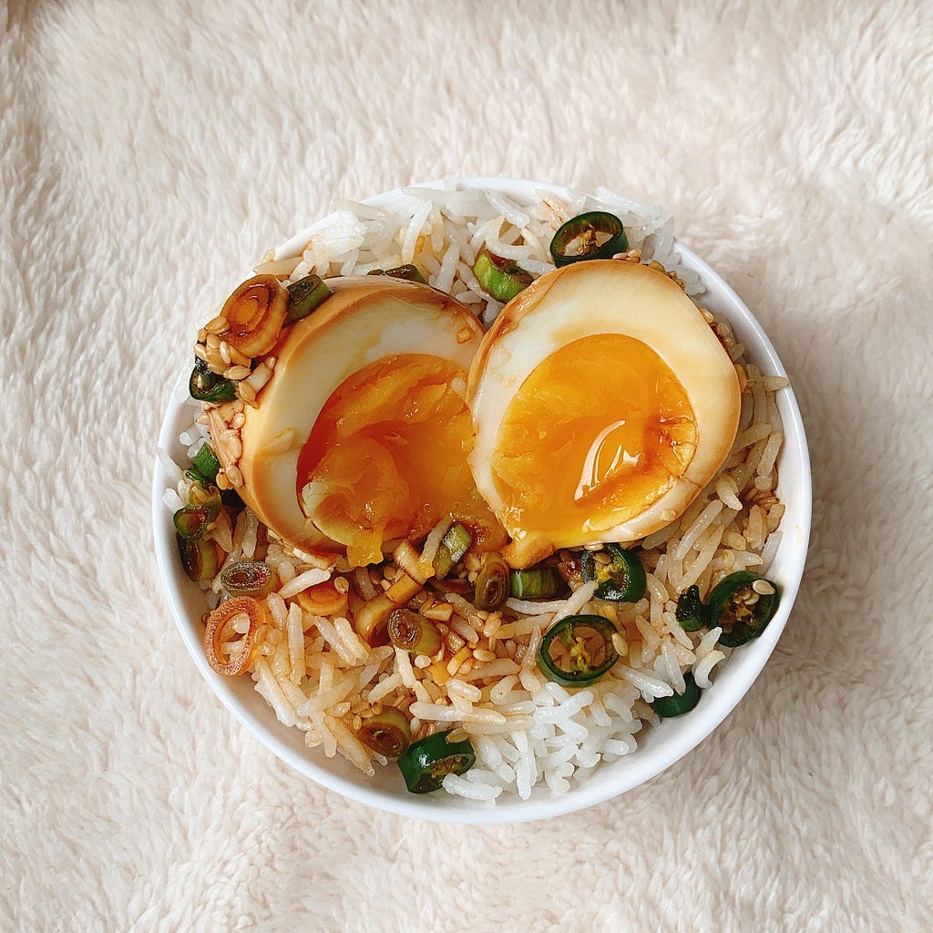 A Close up of Korean Mayak Eggs on a bed of Steamed Basmati Rice. Softboiled marinated eggs are the perfect texture on steamed rice. This dish is Tangy, Spicy, Sweet and Salty at the same time & is perfect on the palate.