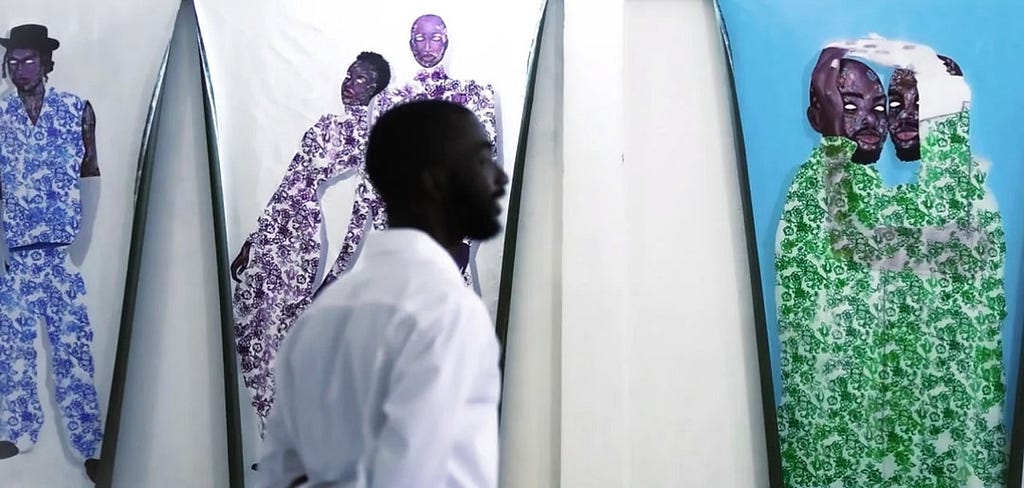 A photograph of Taku walking in front of two of his portraits.