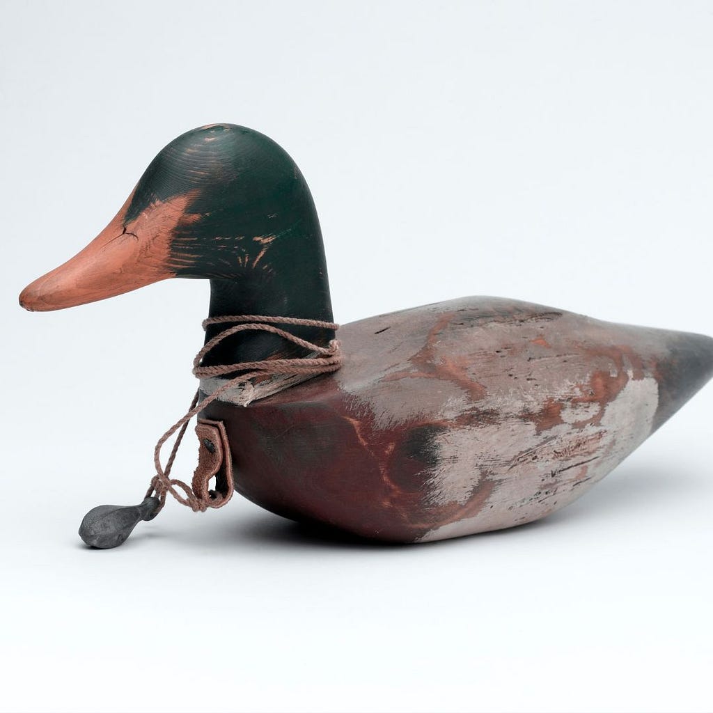 a wooden duck decoy with string around its neck on a plain background