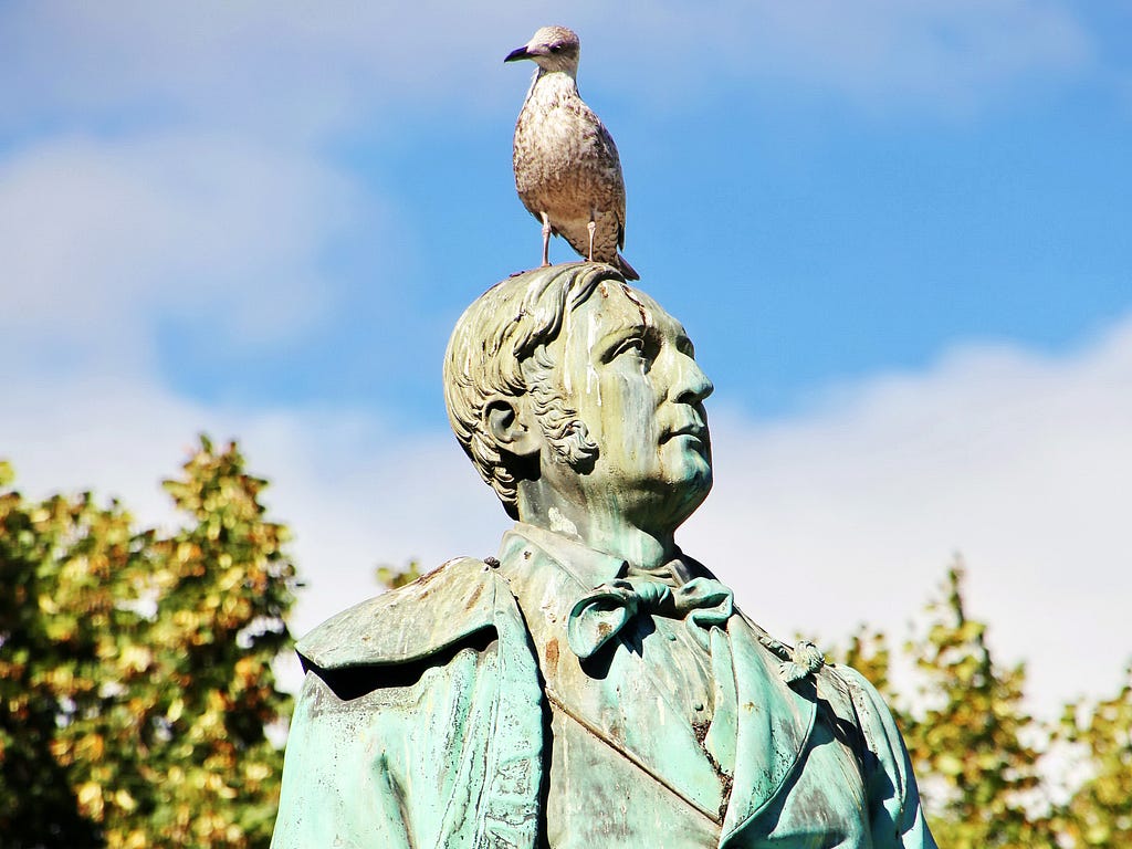 A statue of a prominent man,  with a live seagul on his head.