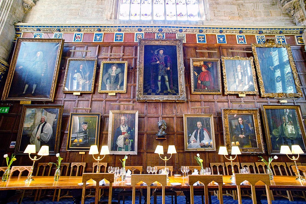 a long dining table with a wall of painted portraits behind it