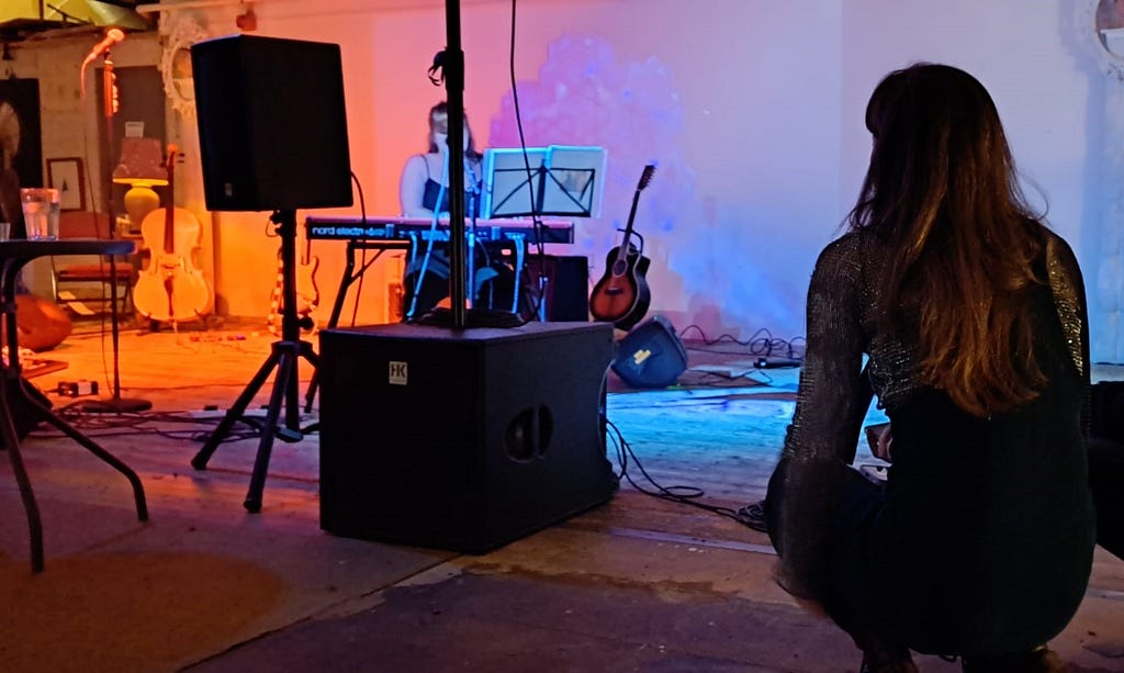 Photo shows the image of a person from behind who is watching someone perform the keyboard from behind a pole