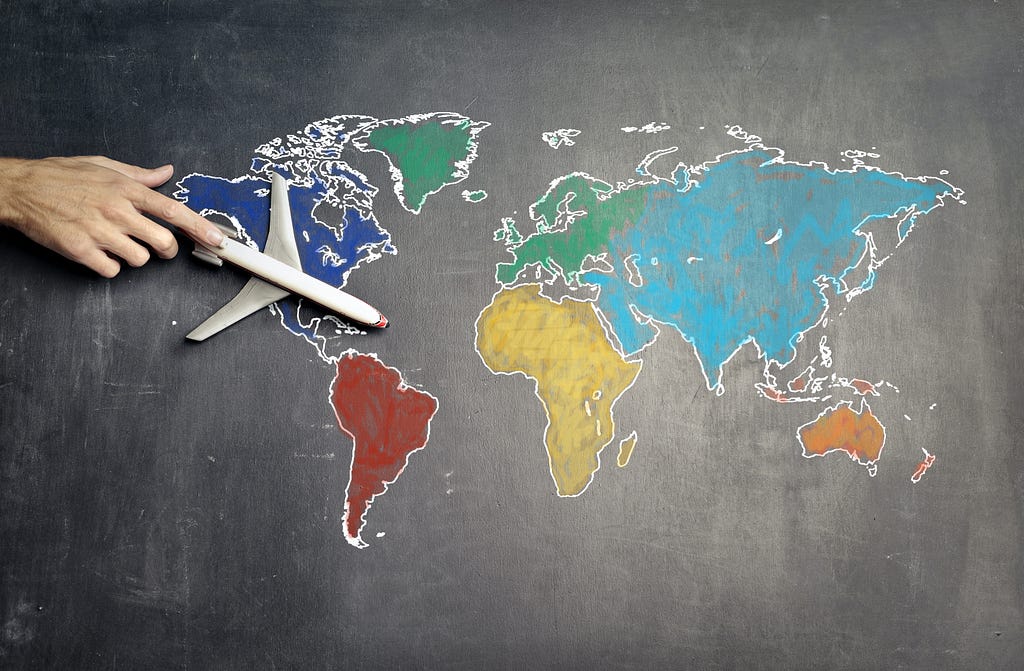 Photo of a map of the world with a hand holding a toy plane.