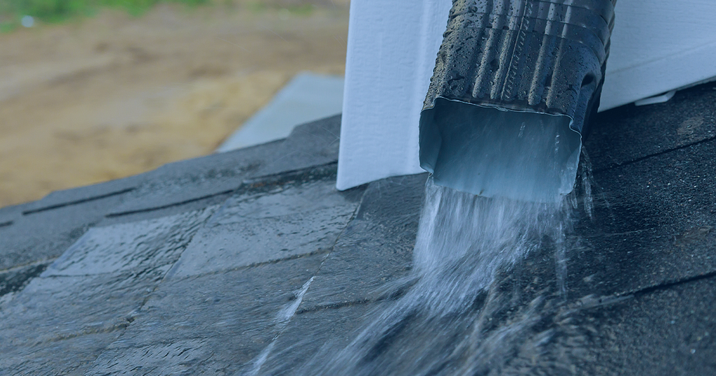 Picture showing rainwater pouring out of a gutter down pipe onto a lower rooftop