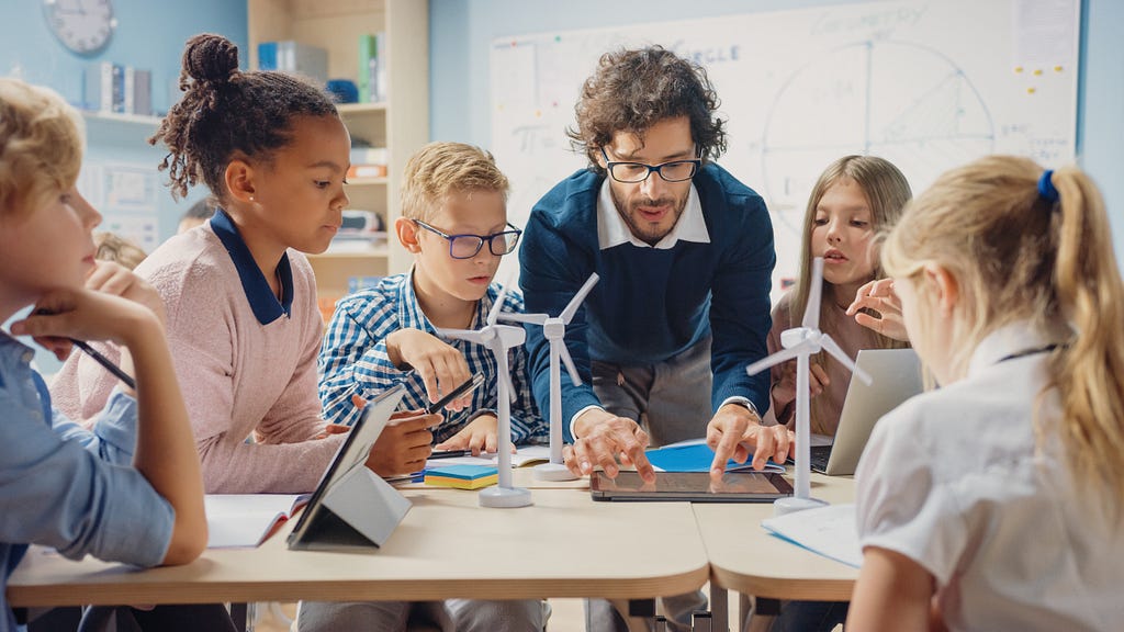 Enthusiastic Teacher holding tablet computer explains lesson about wind energy to students