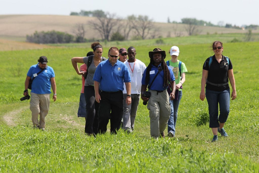 A group of people walk in a field. The first four of the group wear U.S. Fish and Wildlife Service uniforms.