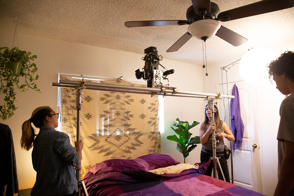 Natalie Perez and another women are putting up a camera above a bed with stands to create a bird eye view shot.