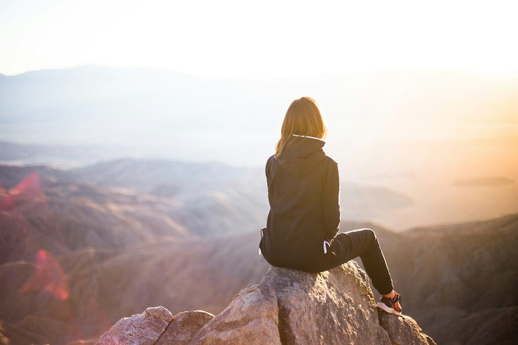 Woman sitting atop a mountain looking at the view around her