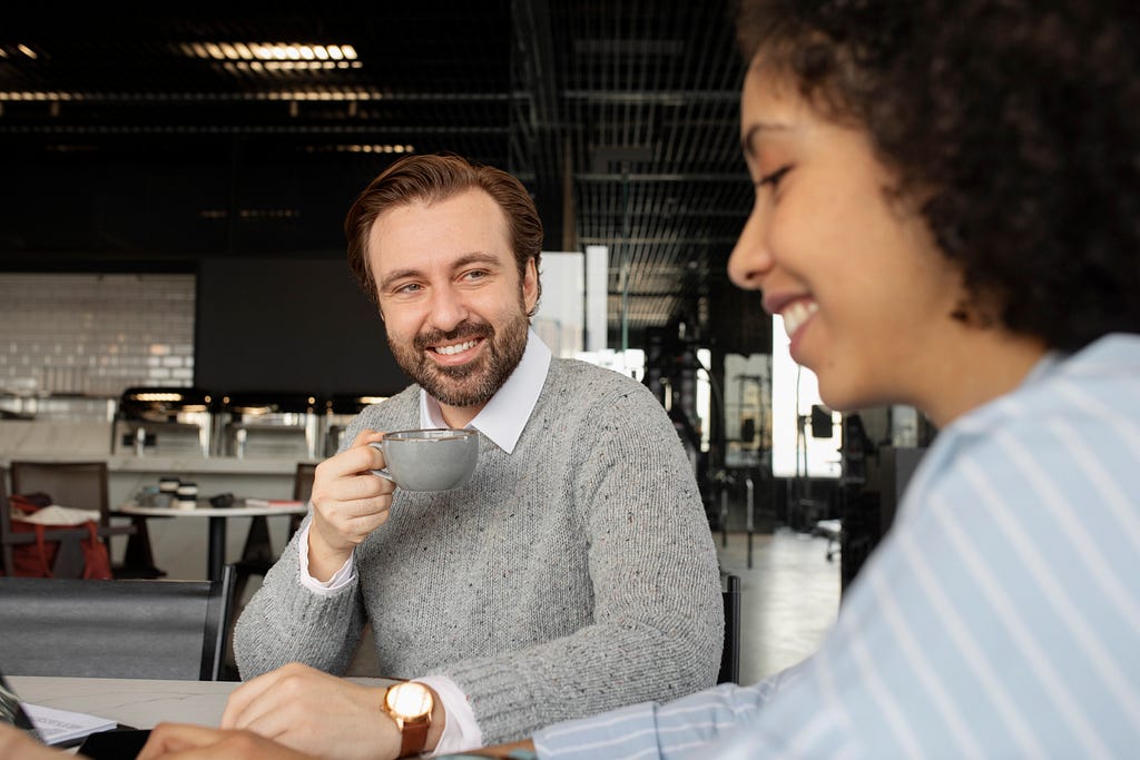 A close-up photograph of two people sitting across in a coffee shop.