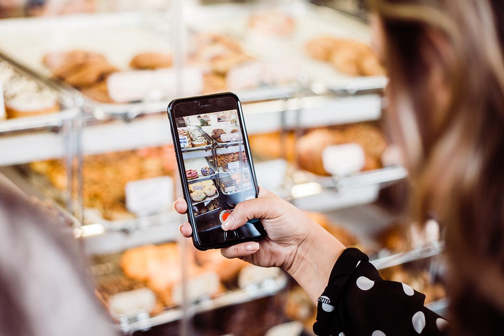 A woman takes a photo of donuts from a shop window with her smartphone.