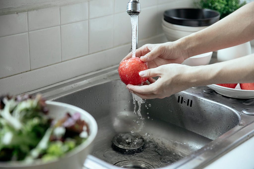 A person washing an apple under running tap water in the kitchen