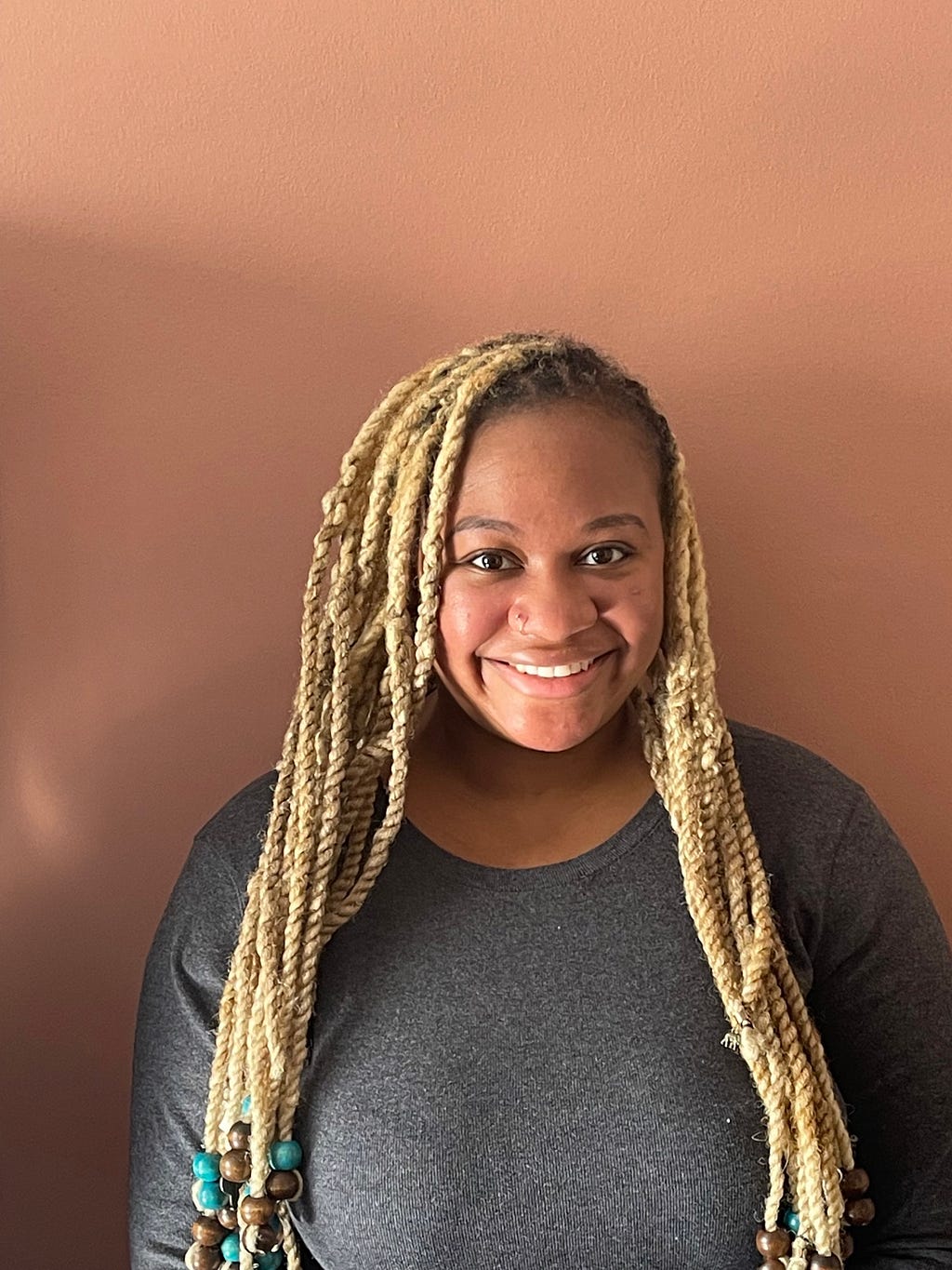 A woman standing and smiling at the camera with a brown background.