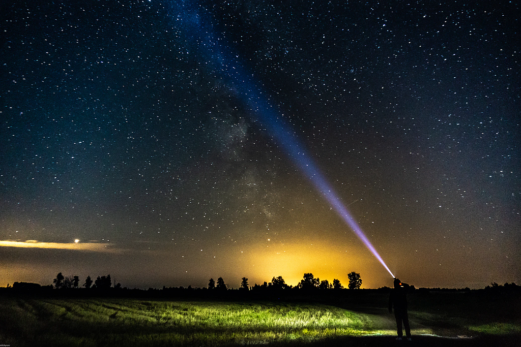 A flashlight beam shines from an outdoor setting at dusk into the starry sky.