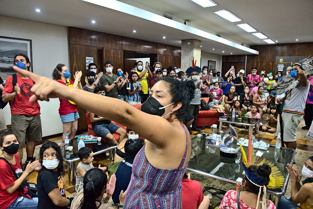 Grupo de manifestantes dentro da Reitoria da UFRGS, indígena em primeiro plano aponta para algo fora da imagem.