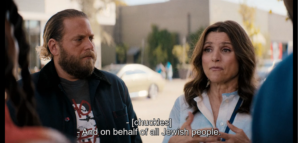 A woman with wide eyes gestures towards figures in the foreground. Subtitles read, “And on behalf of all Jewish people.”
