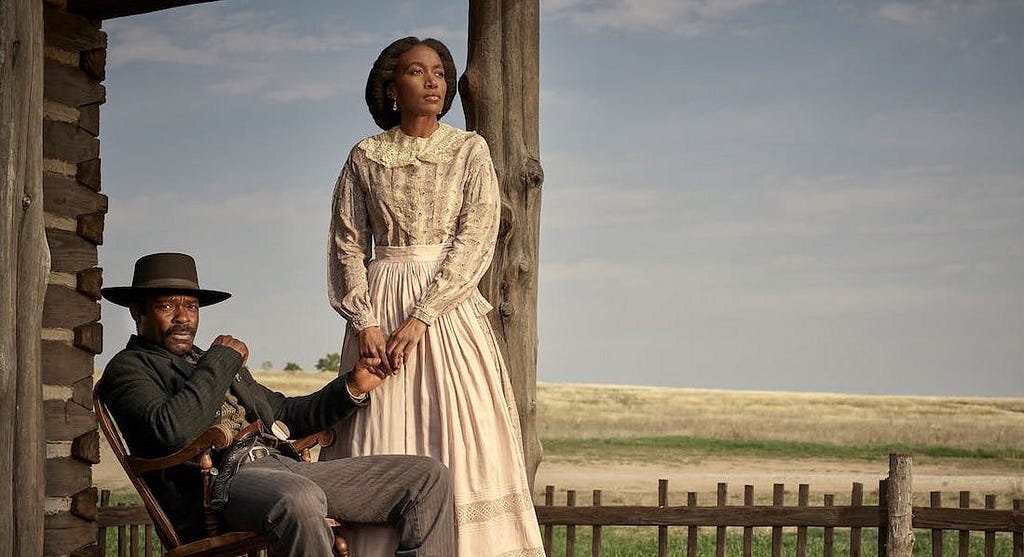 David Oyelowo and Lauren E. Banks as Bass and Jennie Reeves. He sits in a rocking chair while she stands beside him, holding his hand. They are on a porch, and the plains spread behind the fence in the foreground.