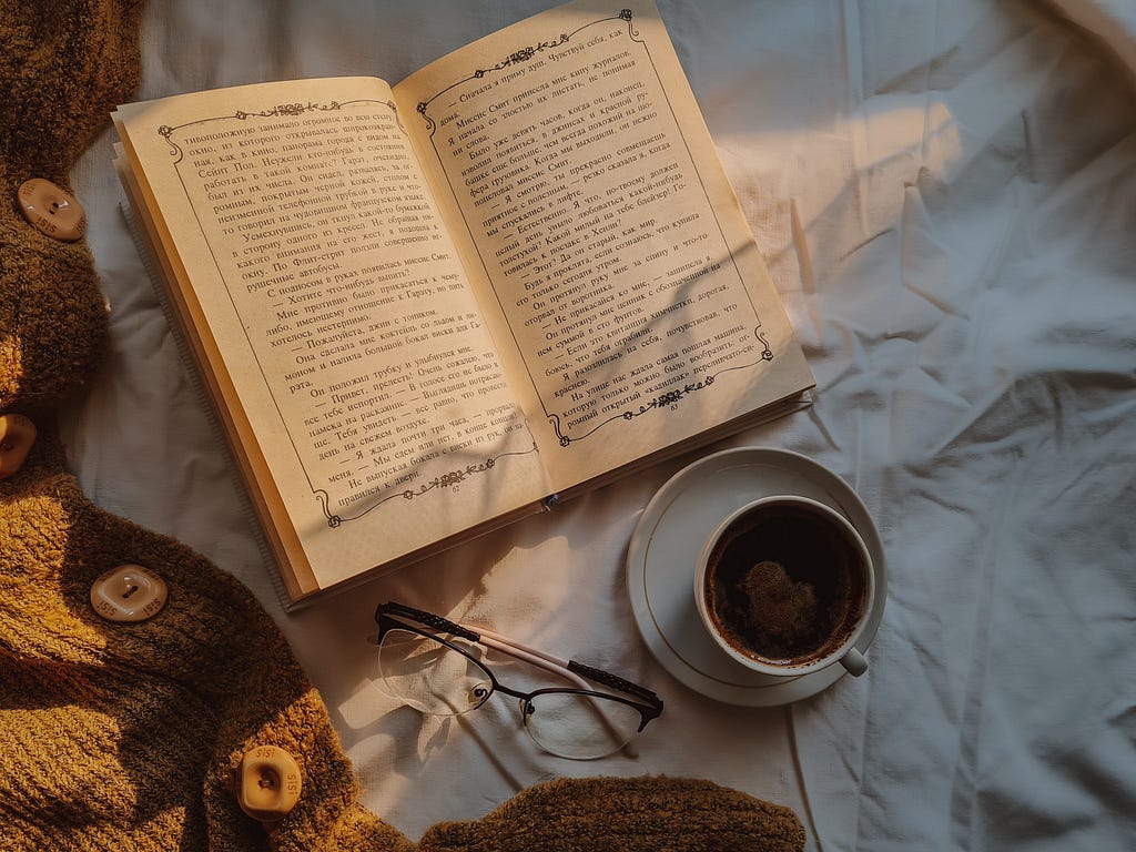 open book on blanket by a pair of glasses and mug of tea
