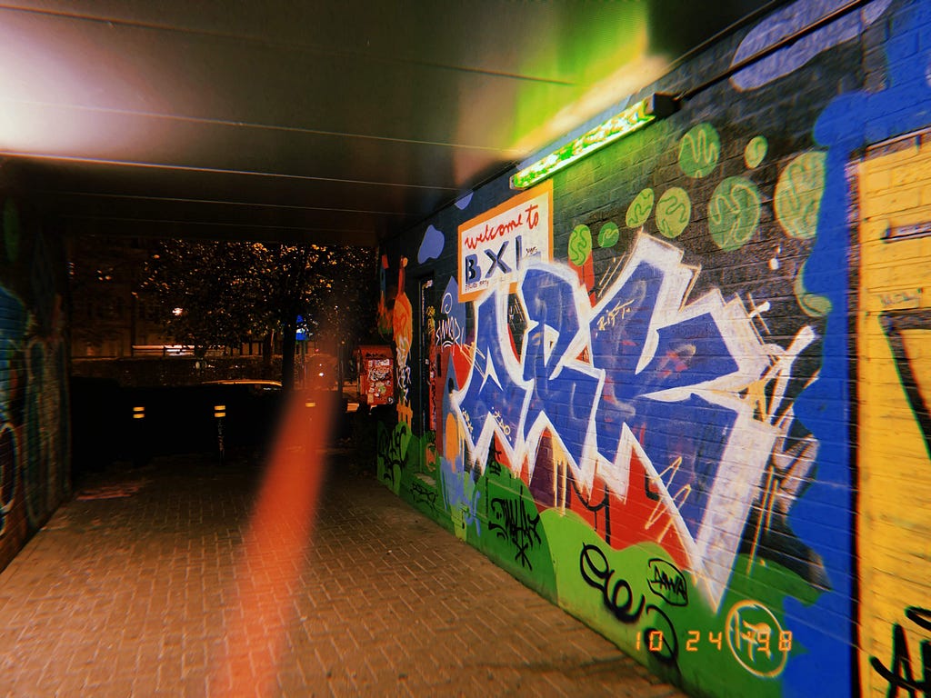 Colorful street art mixed with graffiti in a metro station at night.