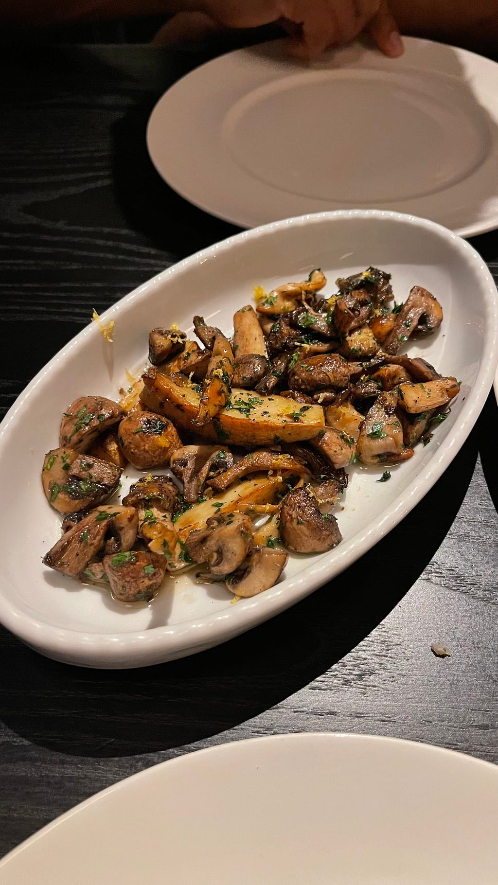 A white plate with sauteed mushrooms and potatoes on a black table