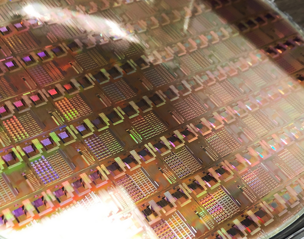 A shiny silicon wafer with many repeating patterns and rainbow coloration on it.