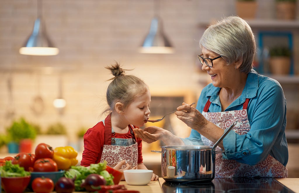 A grandmother cooks in a kitchen with her granddaughter in a family lifestyle portrait session