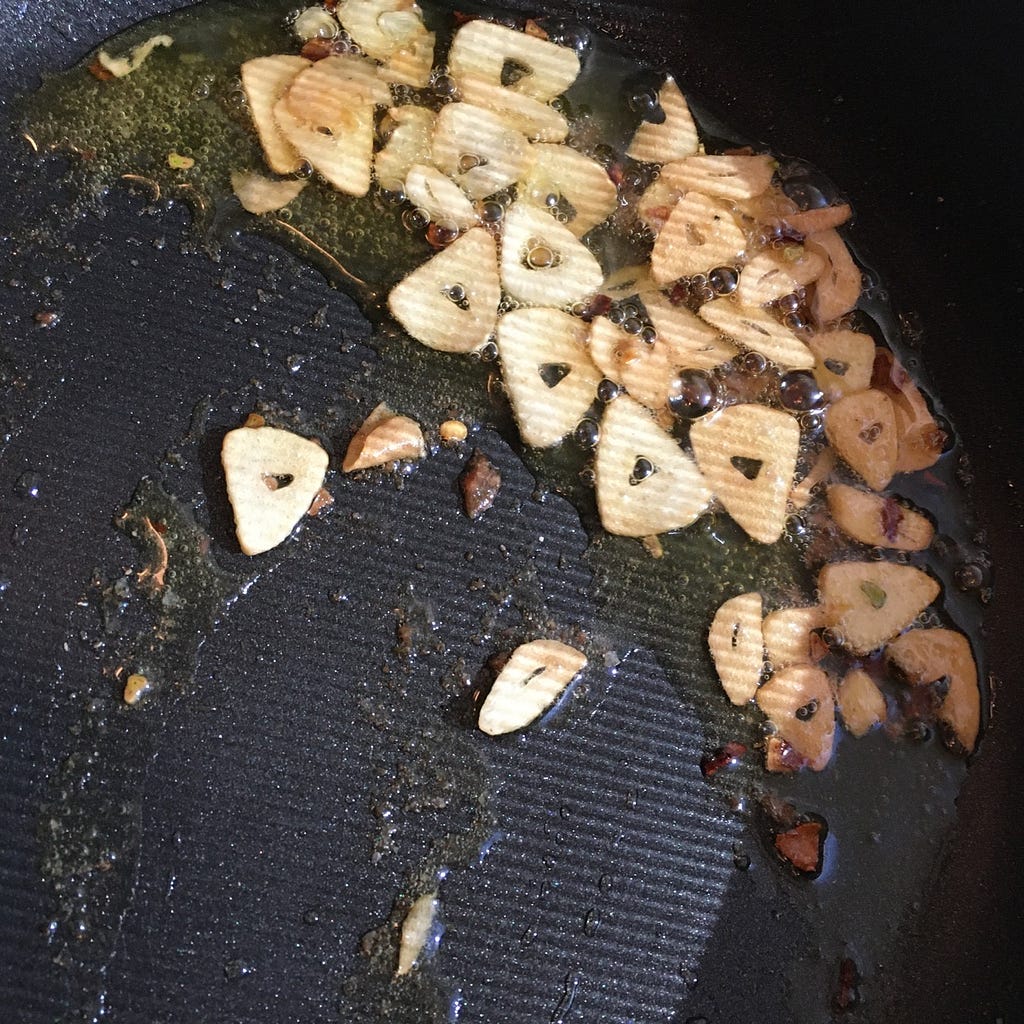 Thin, triangular slices of anchovies cooking in oil in a pan.