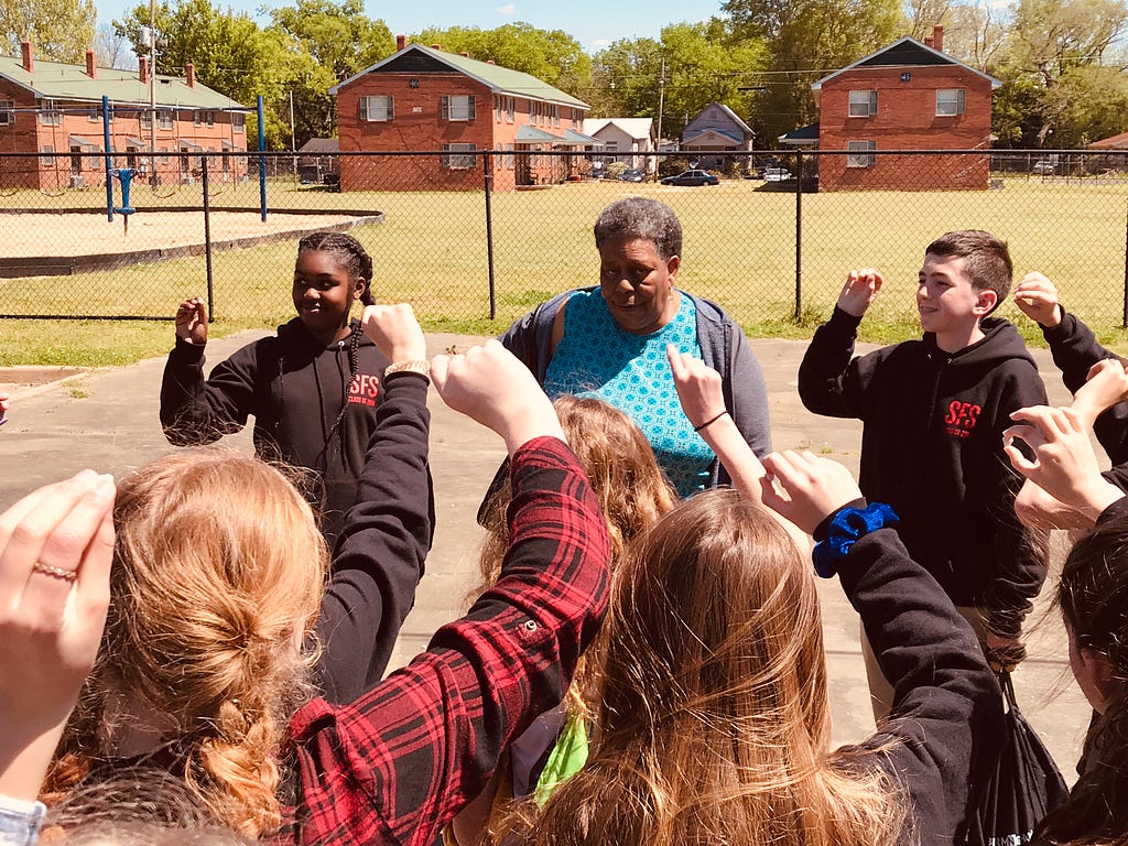 Students standing in circle with adult woman with fists in the air