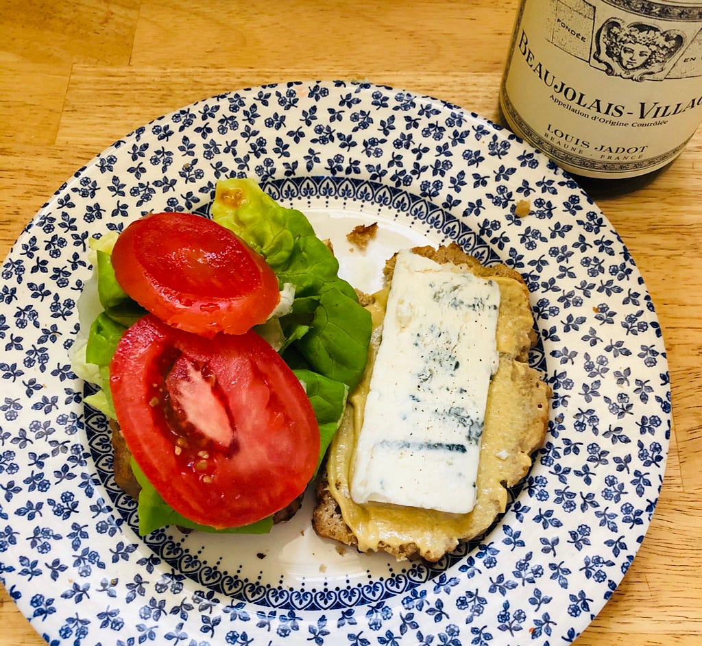 Open gorgonzola sandwich with Dijon mustard, tomatoes, and butter lettuce, on a plate next to a bottle of Burgundy wine.