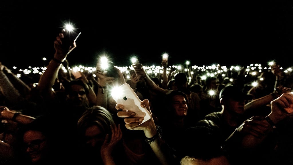 Audience at night holding iphones up with flashlight on