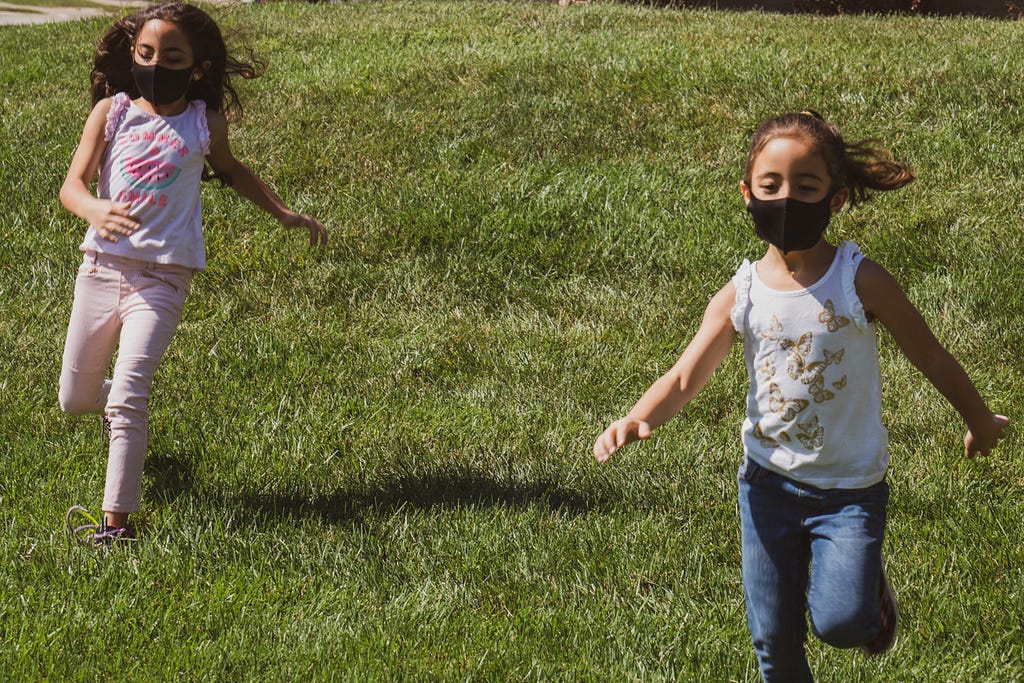 Two young children play outside while wearing COVID-19 face masks.