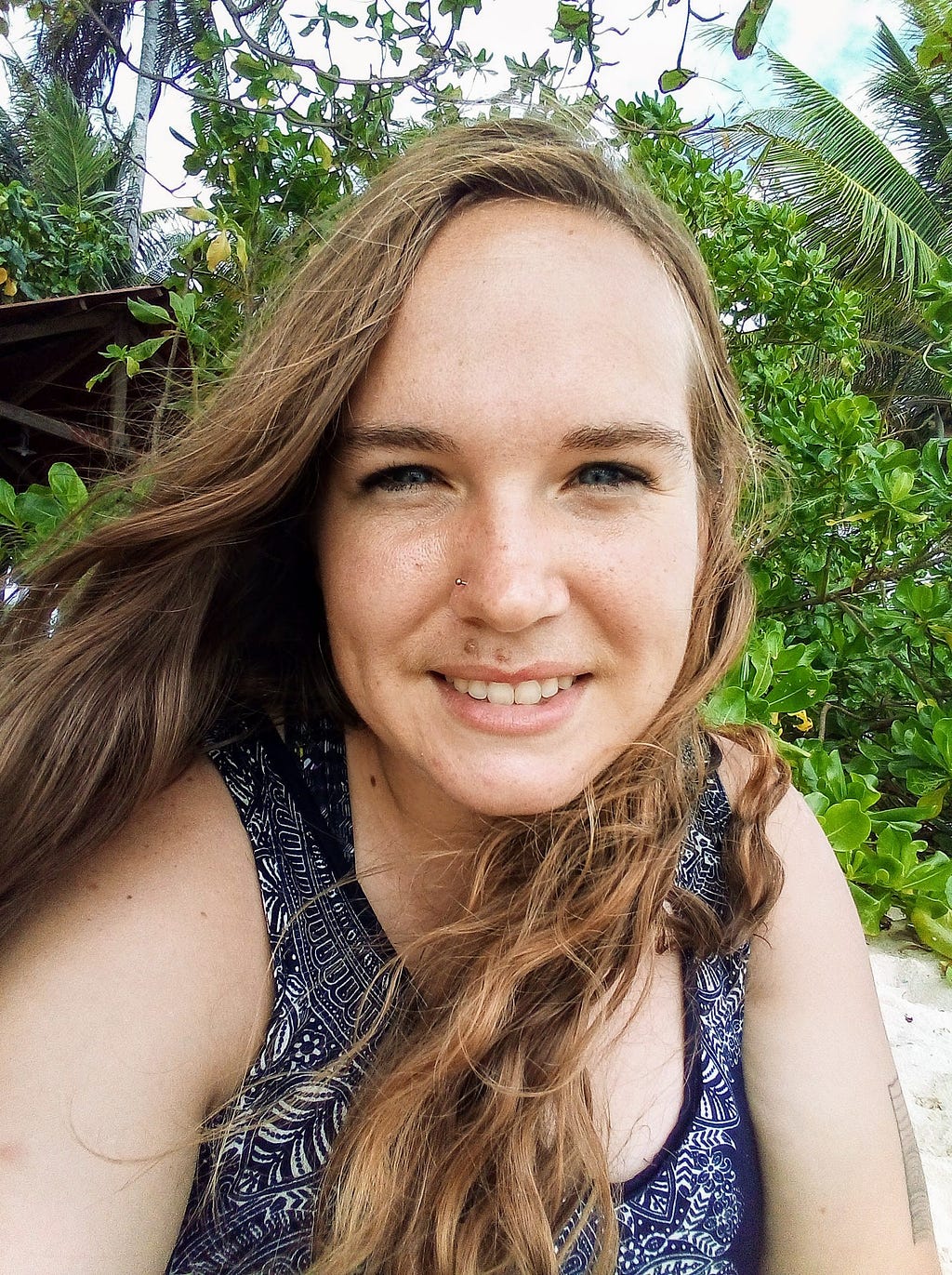 A portrait of Heidi Stewart smiling on a beach with foliage in the background.