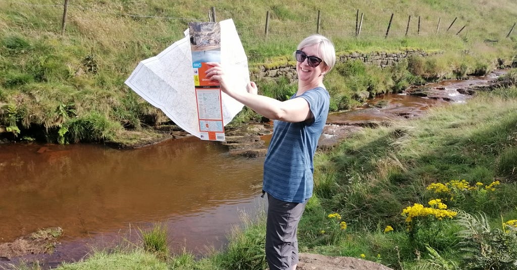 Photograph of the map curator in a field, unfolding an Ordnance Survey map