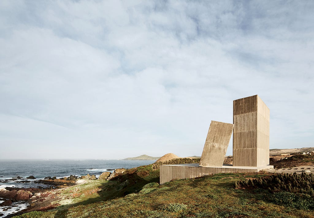 Three angular concrete forms sit on a cliff top.