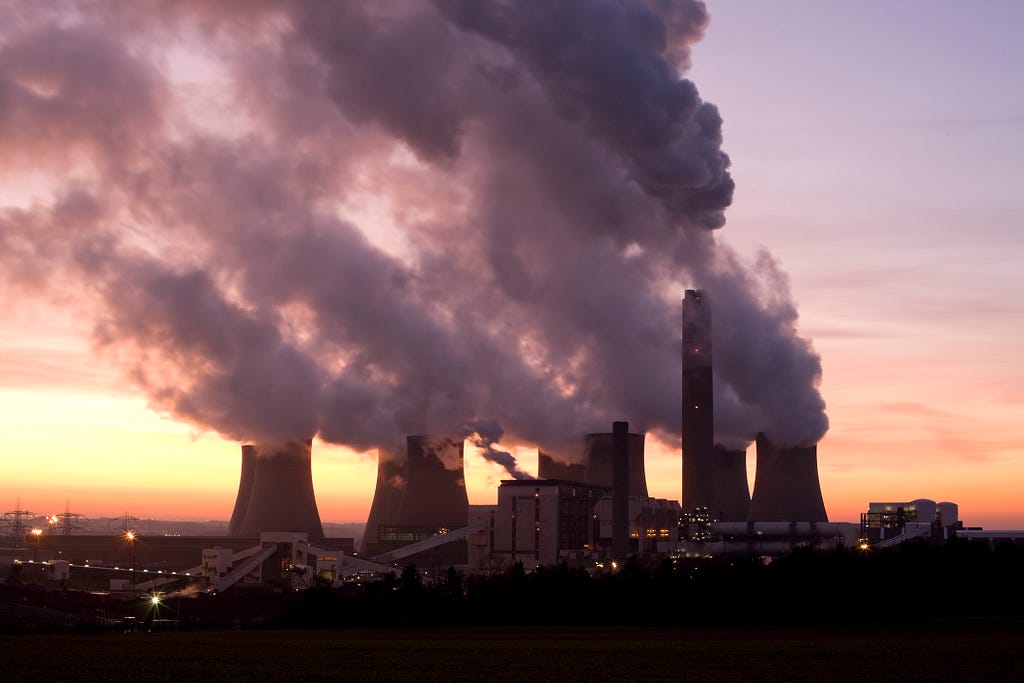 A coal-fired power plant billowing gases into the sky at sunrise