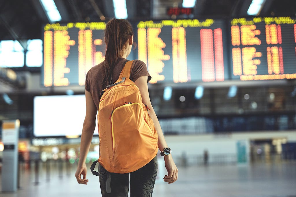 Woman with backpack in an empty terminal, looking at a marquee of flight times.