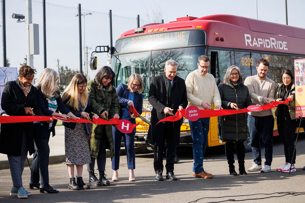 Executive Constantine and community leaders cut a red ribbon in front of a Metro bus, celebrating the launch of the RapidRide H Line.