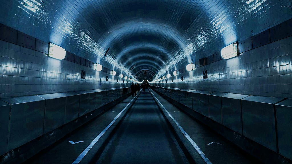 Track-level view of a subway tunnel perspective receding into the distance, with perimeter lights along the path